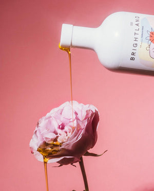a bottle of brightland oil being poured on a pink rose