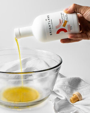 a person pouring brightland awake olive oil into a mixing bowl