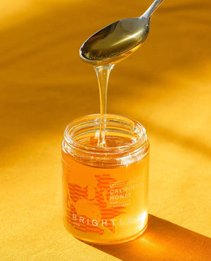 a spoon drizzling honey back into a jar of brightland california honey