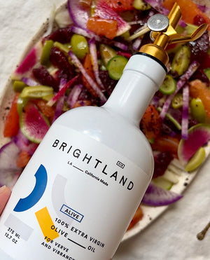 a bottle of brightland alive olive oil being poured onto a salad