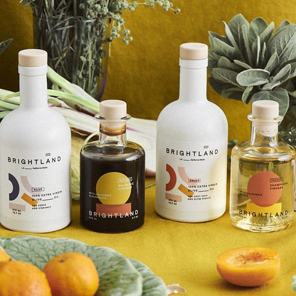 an assortment of brightland oils and vinegars on a table with fruits, vegetables, and plants